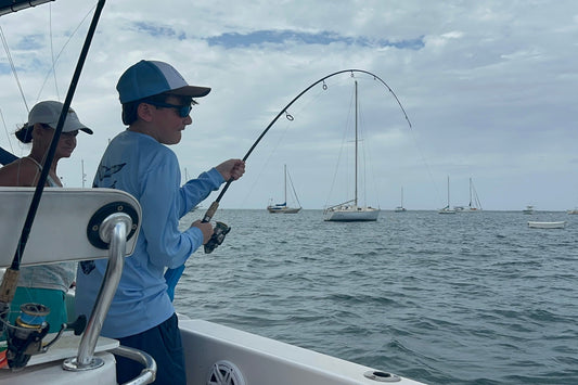A person fishing from a boat with a bent fishing rod, with several sailboats in the background on St.Croix, USVI. Inshore/Near Shore Fishing Charter in St Croix