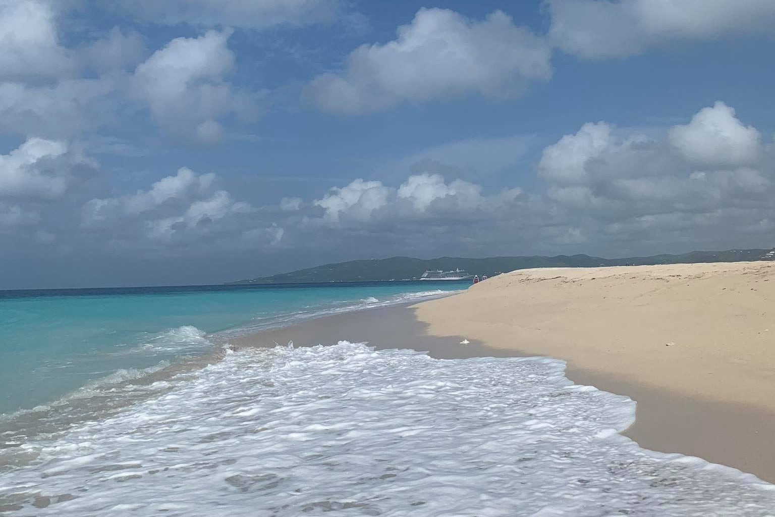 A St.Croix beach scene with blue sky, white clouds, sand, and turquoise ocean water. Sandy Point Beach