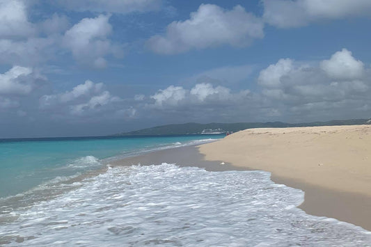 A St.Croix beach scene with blue sky, white clouds, sand, and turquoise ocean water. Sandy Point Beach