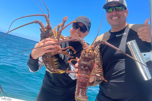 2 People holding 2 lobsters caught on a boat.
