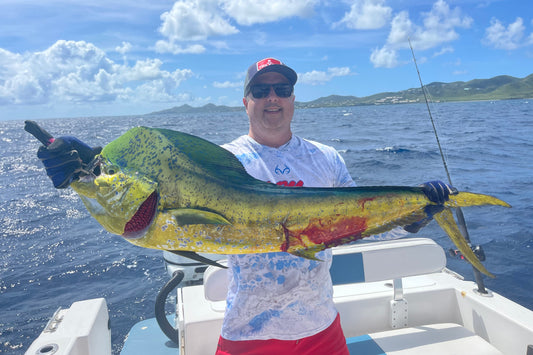 A person on a boat holding a large fish (mahi) with the St.Croix ocean and sky in the background, indicating a successful fishing trip. St Croix Offshore Fishing Charter 